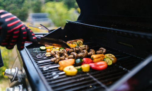 Vegetables on kebobs being cooked on a propane grill.